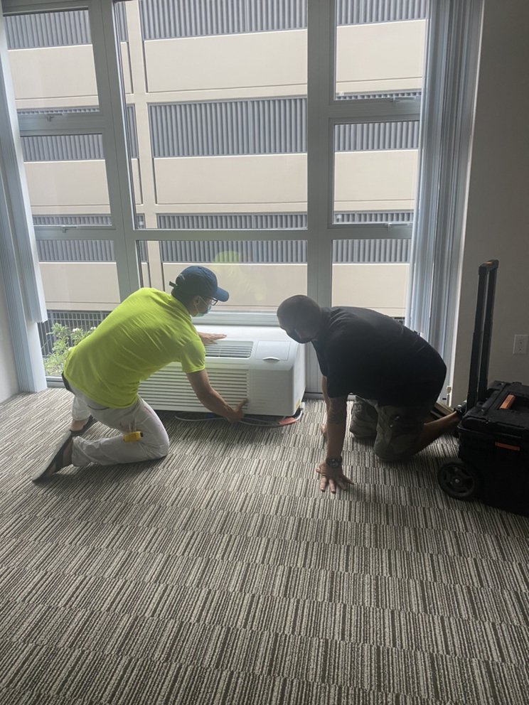 TAKEO SERVICES crew installing a wall AC unit on a job site in Hawaii