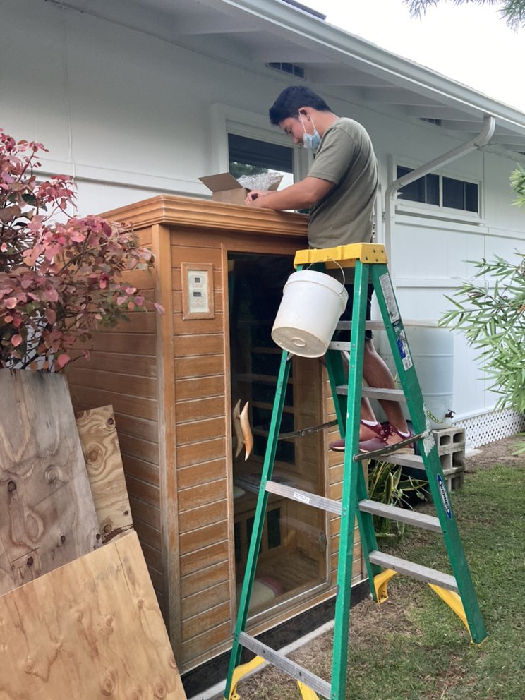 TAKEO SERVICES technician on a ladder assembling a sauna cabinet outside a Hawaii home